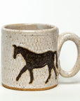 The Faire Ceramic Mug features a black horse silhouette on a speckled beige surface. Its large handle offers practicality and style, is microwave safe, and complements any plain white backdrop.