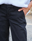 A person wearing ankle length black Frank & Eileen Westport Italian wide leg pants and a white knit sweater stands outdoors with one hand in their pocket.