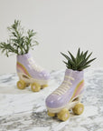 Two Accent Decor Rollerskate Planters in pastel purple with yellow wheels, each holding a small green plant, sit on white and gray marble—a quirky accent and perfect gift for plant lovers.
