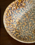 The Walden Bowl by Accent Decor features intricate textured patterns in cream, brown, and blue, adding sculptural flair to any space when displayed on a wooden surface.