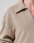 A close-up of a person wearing the Citizens Of Humanity/AGOLDE trapeze pullover—a beige, collared, long-sleeve sueded fleece with a relaxed fit. The image highlights the upper chest, shoulder area, open collar, and soft texture.