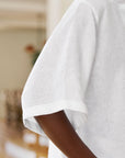 Close-up of a person wearing the Frank & Eileen ROSIE SS Button Up F25—a versatile, loose-fitting white linen short sleeve shirt. The focus is on the arm and sleeve against a softly blurred background.