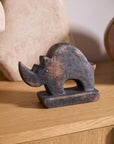 The Accent Decor Rhino Sculpture features a small, dark-speckled design with a curved back and large horn, making it a striking accent on any wooden surface alongside neutral decor.