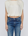 A person faces forward with arms relaxed at their sides, wearing the Moussy MV Satin Shell Cap Top in off-white and blue jeans. The background is plain light gray.