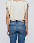 A person is seen from behind wearing the Moussy MV Satin Shell Cap Top—a light-colored, short-sleeved blouse—paired with blue jeans against a plain, light gray background.