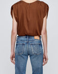 A person stands with their back to the camera, wearing the Moussy MV Satin Shell Cap Top in brown, tucked into high-waisted, faded blue jeans featuring visible back pockets and a tan leather patch on the waistband.