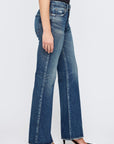 A person wearing Moussy's Lismore 70’s Flare high-waisted blue jeans with frayed hems and black pointed-toe heels, standing against a plain white background.