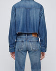 A person wearing the Moussy Foley Shirt, a cropped denim button-down, with blue jeans, viewed from the back against a plain light background.