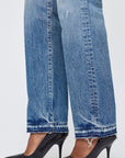 A person wearing Moussy's Dorchester Straight blue mid-rise, slightly distressed wide-leg jeans with frayed hems and black textured pointed-toe heels, standing on a white background.