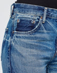 A close-up of a person wearing Moussy's Holyoke Panel Wide lightweight, faded blue jeans featuring a dark patch on the front pocket and a black top tucked in.