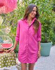 A woman in a bright pink Frank & Eileen MARY Shirtdress S25 smiles outdoors by a table with polka dots, watermelon, and a drink, framed by lush green plants and bold pink decor—a standout style moment.