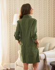 A woman, back to the camera, wears the Frank & Eileen Southern Dress in green Italian Performance Linen. She stands in a cozy room with a beige armchair, floor lamp, and patterned wallpaper evoking Southern Ireland charm.