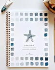 The Faire "Watercolor Workbook" features a spiral-bound design with beginner-friendly illustrations. A central starfish is bordered by blue and gray watercolor squares, accompanied by a paint tube, paintbrush, and shell-filled bowl for a serene scene.
