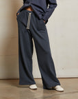 A person wears the Perfectwhitetee French Terry Pant in navy—loose, straight-leg, 100% cotton with patch pockets and a drawstring waist—paired with a navy shirt and white sneakers on a concrete floor.