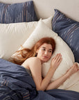 A woman with red hair lying comfortably in a bungalow in Scottsdale, Arizona, partially covered by a Morel Euro Sham Moon Blue duvet, resting her head on white pillows from Coyuchi Inc.