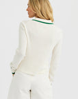 A woman with loose blonde hair is seen from the back wearing the One Grey Day Royale Button Up—a white ribbed polo with a green-striped collar—paired with white shorts, standing against a plain white background.