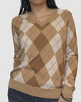 Someone wears the Brazeau Tricot Argyle V-Neck sweater in brown and beige with diamond patterns and thin red and black lines, paired with dark pants against a light, plain background.