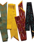 Five vibrant Faire Twilly Scarves are displayed side by side, featuring bold geometric and illustrated patterns—including a striking horseshoe design—in green, yellow, red, and black. Perfect as a unique gift silk scarf.