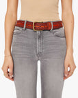 Wearing The Eye Opener beige sleeveless top by Mother with light gray high-waisted jeans and a vintage leather belt with brass buckle, hands relaxed at sides adorned with delicate rings and bracelets.