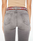 A person shown from the back wears The Eye Opener by Mother—a beige sleeveless top, gray jeans, and a colorful patterned beaded leather belt with "MOTHER" visible on the waistband.