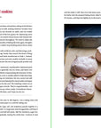 A close-up of six light pink strawberry meringue cookies with cracked tops on a parchment-lined baking sheet, alongside an easy "strawberry cloud cookies" recipe inspired by Smitten Kitchen Every Day from Random House.