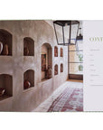An open spread of "Natural Living by Design" by Hachette Book Group displays beige walls with built-in shelves of clay pottery and a contents page, all set on a patterned rug in sunlight for a fresh, healthy home feel.