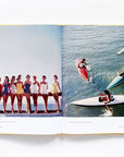 An open book, "Slim Aarons: Women" by Hachette Book Group, displays vintage photos: on the left, elegant women in swimsuits pose on a dock; on the right, people paddle boats and canoes under sunny skies.