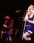 A prismatic, double-exposure photo with vivid colors from "Blondie In Camera 1978" by Simon & Schuster Inc. shows a blonde woman singing on stage beside a guitarist, echoing classic Blondie images with motion blur effects.