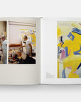An open copy of "Way of Living: Art of Willem de Kooning" by Hachette Book Group shows photos of de Kooning painting on the left and a vibrant yellow, blue, and pink Abstract Expressionism piece on the right.