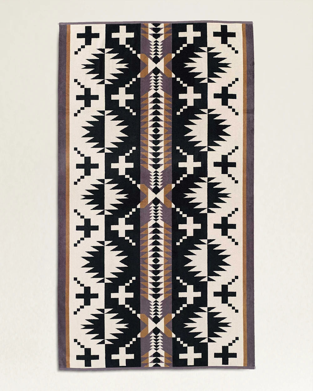 A traditional geometric patterned rug with a symmetrical design featuring black, white, and earth tones, displayed against a bungalow's light textured wall in Scottsdale, Arizona. - 
A Pendleton/Babblitt's Wholesale Spa Towel with a symmetrical design featuring black, white, and earth tones, displayed against a bungalow's light textured wall in Scottsdale, Arizona.