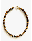The Galleria Necklace by Faire features polished round tiger's eye beads with brown and gold bands, finished with gold plated findings and a small round tag, shown on a plain white background.
