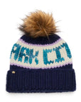 The Faire Knit Ski Hat is a luxury navy blue beanie with a brown faux fur pom pom, bold white and teal "PARK CITY" lettering, a folded cuff, and a small metallic emblem for extra style.