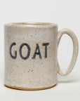 A handmade ceramic mug from Faire, featuring a speckled beige finish and blue "GOAT" lettering, set against a plain white background.
