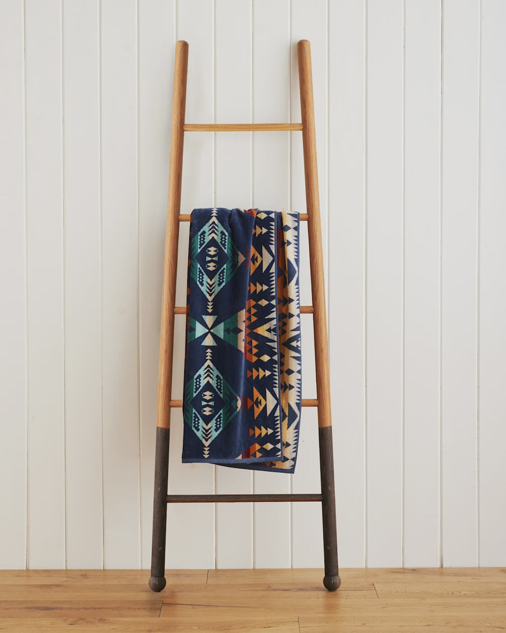 A wooden ladder leaning against a white wall in a Scottsdale Arizona bungalow, with a Pendleton/Babblitt's Wholesale spa towel draped over its middle rung. The spa towel features blue, orange, and white geometric designs.