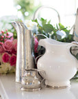 The Vintage 1815 Pitcher by Faire is displayed on a table with pink and white roses and green foliage. Soft natural light highlights the beauty and craftsmanship of this elegant piece.