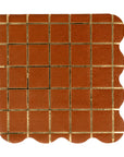 The MME Cocktail Napkin by Faire is a brown square paper napkin featuring a gold grid of small squares, a scalloped right edge, and a subtly textured background.
