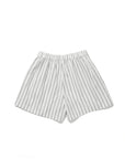 The Limon by Kule: white cotton shorts with vertical black pinstripes and an elastic waistband, shown on a plain white background—ideal for vacation-ready looks.