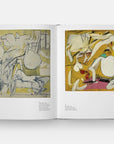 The “Way of Living: Art of Willem de Kooning” by Hachette Book Group lies open, showing two abstract paintings—a pale, sketch-like piece on the left and a vivid yellow composition with organic shapes on the right.