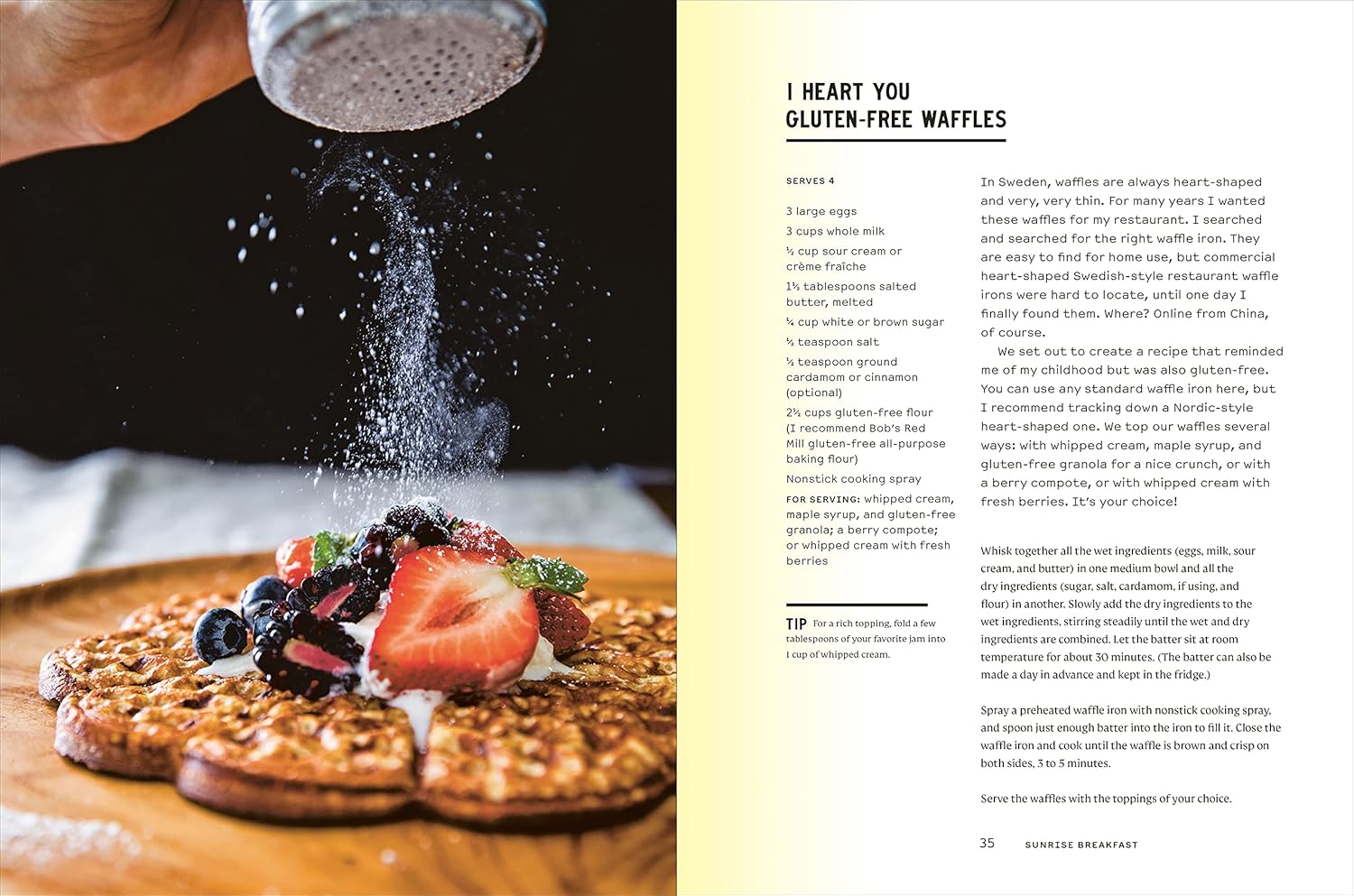 A plate of gluten-free waffles with fresh berries sits on a table as powdered sugar is sprinkled over it, inspired by the Malibu Farm Sunrise dish from Random House, capturing the essence of fresh Southern California cooking.