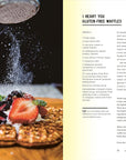 A plate of gluten-free waffles with fresh berries sits on a table as powdered sugar is sprinkled over it, inspired by the Malibu Farm Sunrise dish from Random House, capturing the essence of fresh Southern California cooking.