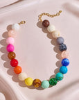 The PERRY Styles Bubble Gum Necklace is a vibrant statement piece for women, featuring large round gradient beads on a gold chain, displayed on pale pink fabric—perfect for adding a boho flair to any outfit.