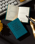 Teal Definately Not my Passwords Tiny notebook by Hachette Book Group open on desk beside keyboard and flower.