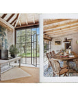 Open to "Natural Living by Design" from Hachette Book Group: one page shows a sunlit room with a desk and tapestry, the other displays a rustic dining area with wicker chairs and an exposed wooden ceiling for healthy living.