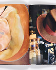 An open book displays a close-up of the Stetson label by Random House on the left page, and a brown hat with a red band on a black stand on the right, evoking classic cowboy culture and heritage.