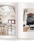 An open copy of "Creating A New Home In Mallorca" by Ingram Book Company displays Malene Birger’s bright studio with abstract black and white art on the left page and a close-up of a black, white, and brown painting on the right.