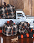 A Faire Pumpkin is displayed as farmhouse decor with a metal toy truck, three plaid pumpkins, and a black and orange felt ball garland, arranged on a wooden surface against a wooden background.