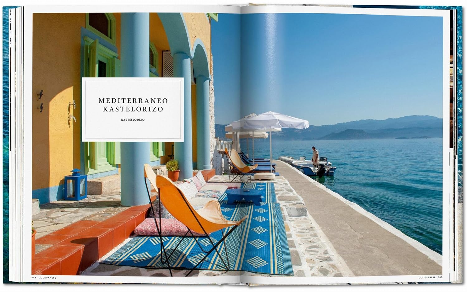 A sunlit terrace with colorful chairs and umbrellas overlooks the calm sea on Kastelorizo, as seen in "Great Escapes Greece The Hotel Book" by Ingram Book Company—featuring serene landscapes, a docked boat, and distant mountains.