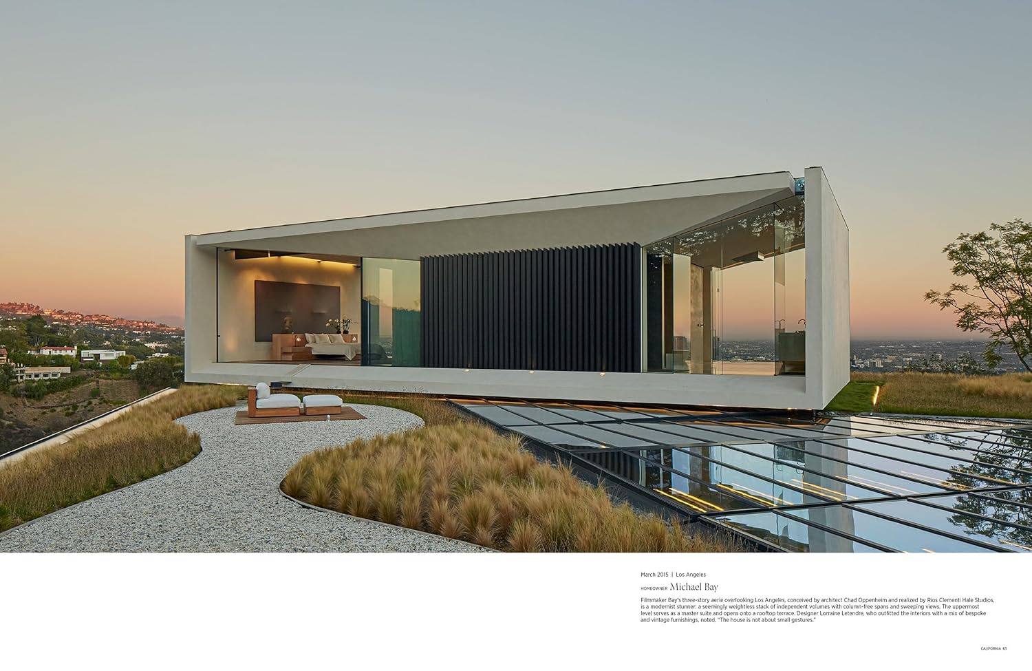 A modern glass-walled house with a cantilevered design overlooks a sunset-lit hillside, its stunning interior visible through floor-to-ceiling windows—echoing the style showcased in "Architectural Digest at 100" from Hachette Book Group.