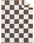 The Faire Double Sided Hand Towel features a brown and white checkerboard waffle weave design. One corner is folded to show the reverse side, with a visible small tag in the bottom right.