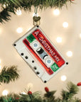 The Old World Ornaments by Faire features a cassette tape labeled "A Christmas Mix," hanging among assorted decorations on a lit tree branch.